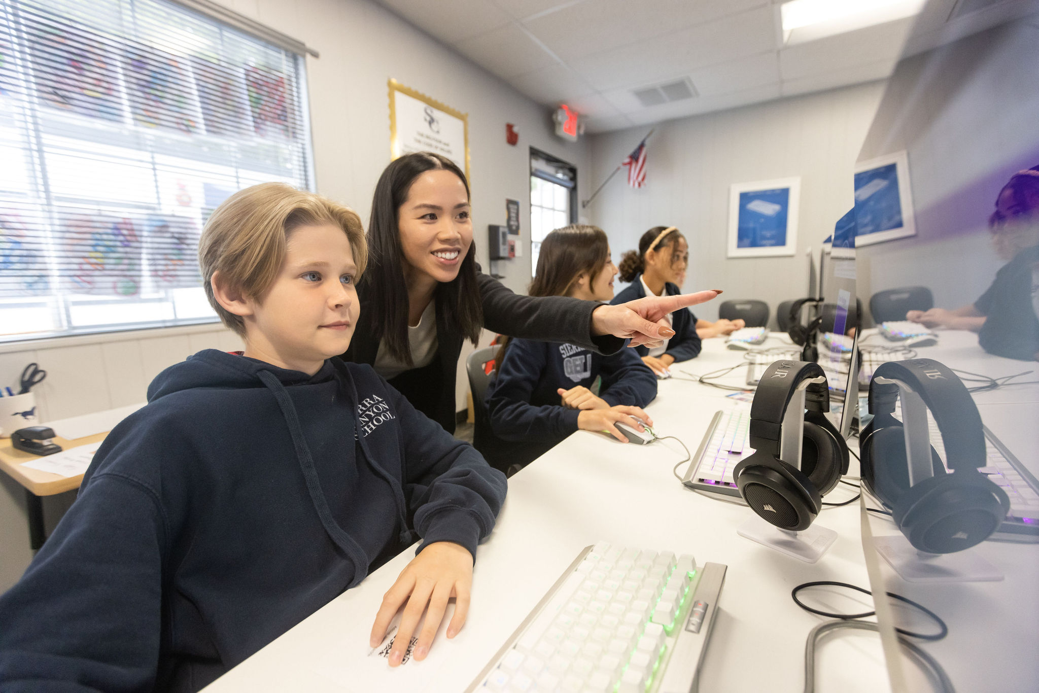 A lower school teacher and two students from Sierra Canyon are focused on their computers in a classroom.