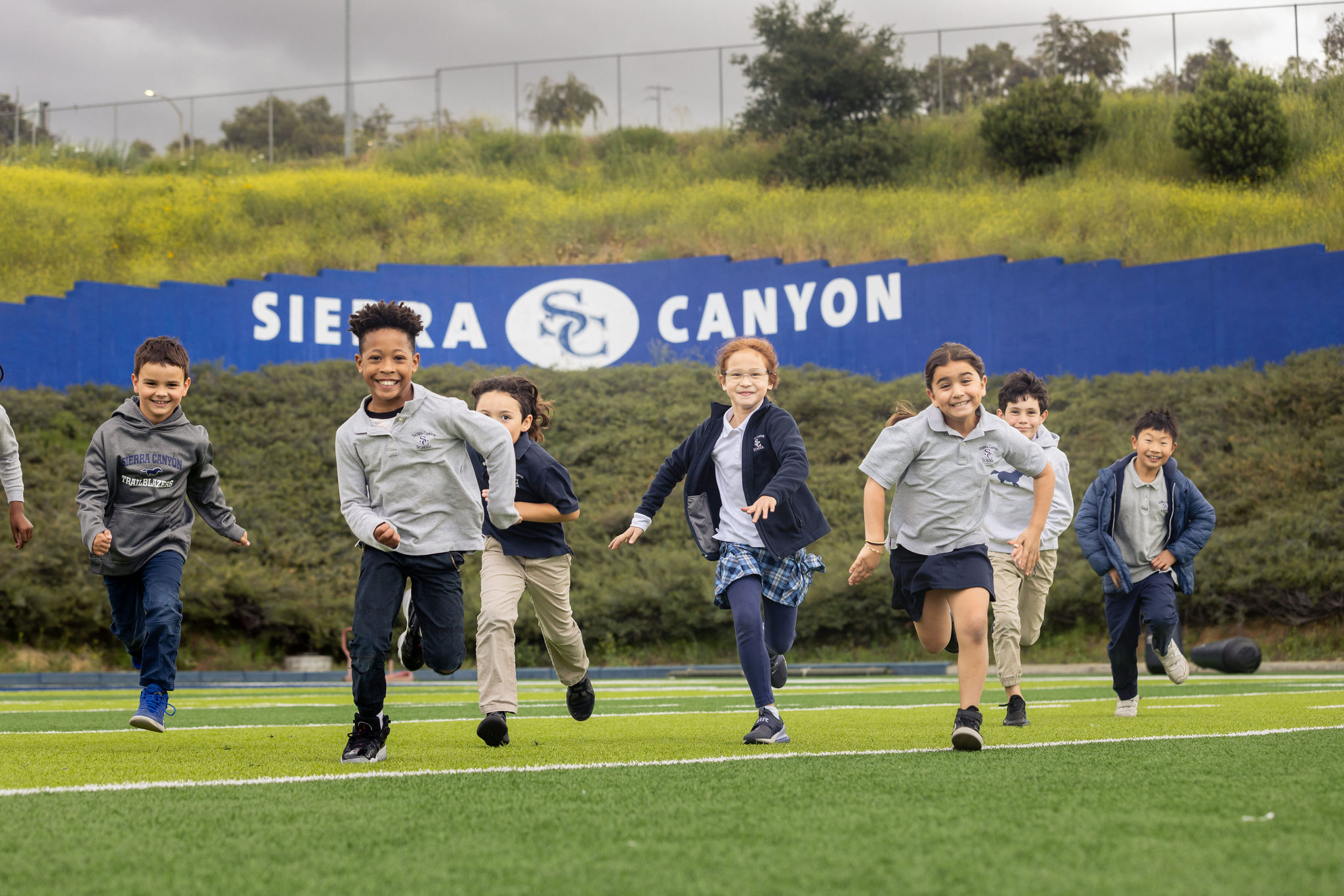 A group of kids running on a field with a sign that says Sierra Canyon. Support the school annual fund!